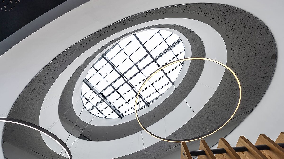 Blick nach oben auf das LAMILUX Glasdach im Kompetenzzentrum Breisgau mit moderner Ringbeleuchtung und architektonischem Atrium.