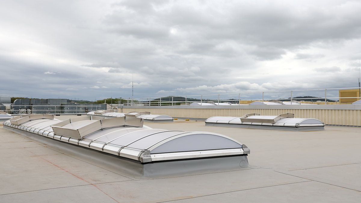 Flachdach mit mehreren neuen Dachoberlichtern und grauem Himmel im Hintergrund.