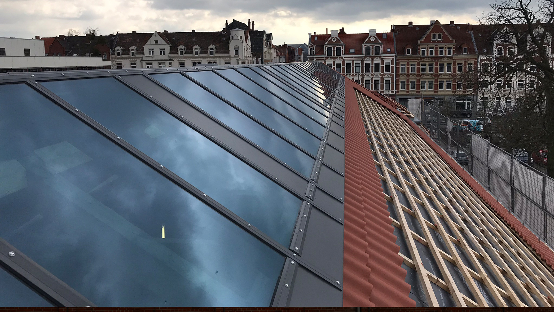 Modernes Glasdach mit einem roten Ziegeldach in Bauphase an der Leibniz-Universität Hannover, mit historischen Gebäuden im Hintergrund.