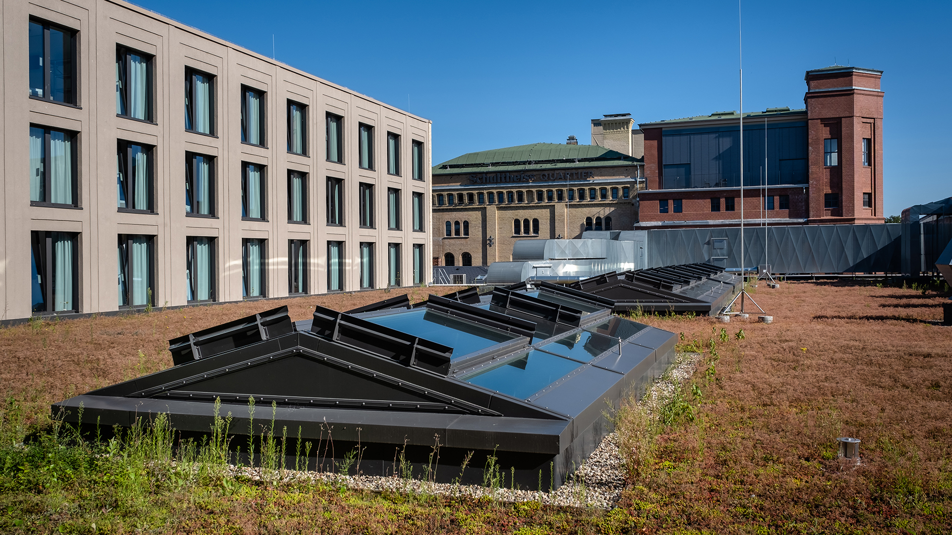 Dachbegrünung des Schultheiss Quartiers in Berlin-Moabit mit Glasdächern und modernem Gebäudekomplex im Hintergrund.