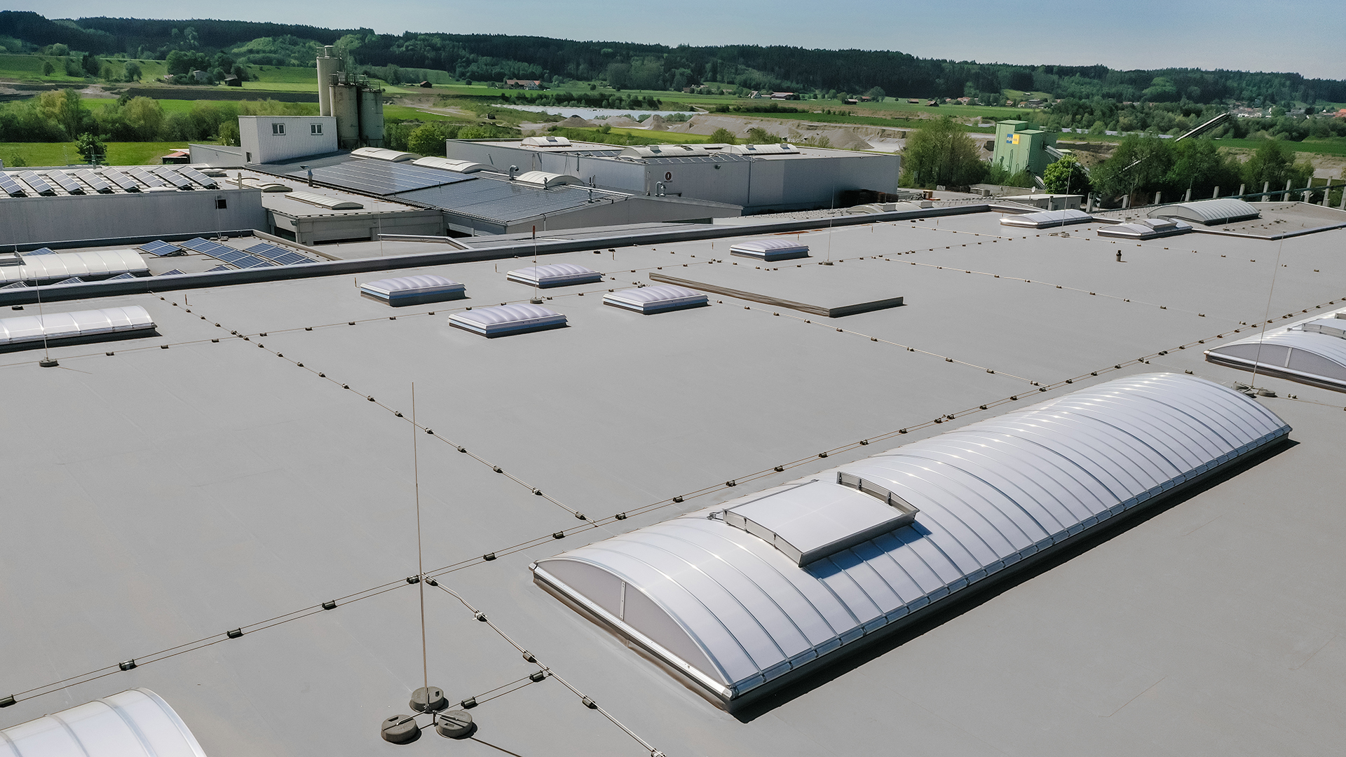 Luftaufnahme der Produktionshalle des Bauunternehmens Unglehrt mit LAMILUX Lichtkuppeln F100 W, Lichtbändern B und Solarpaneelen auf dem Dach.